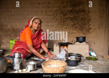 CHIKHALDARA, MAHARASHTRA - Agosto 28, 2018: Un misterioso vecchio donna fare e cucina / cottura di alimenti freschi in un villaggio rurale in una cucina vintage u Foto Stock