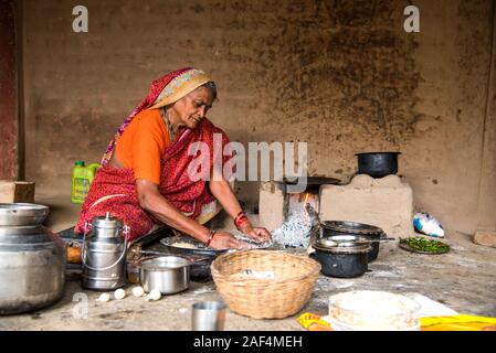 CHIKHALDARA, MAHARASHTRA - Agosto 28, 2018: Un misterioso vecchio donna fare e cucina / cottura di alimenti freschi in un villaggio rurale in una cucina vintage u Foto Stock