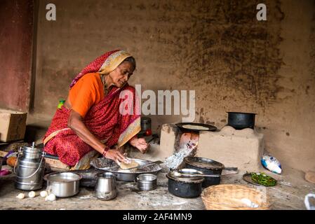 CHIKHALDARA, MAHARASHTRA - Agosto 28, 2018: Un misterioso vecchio donna fare e cucina / cottura di alimenti freschi in un villaggio rurale in una cucina vintage u Foto Stock