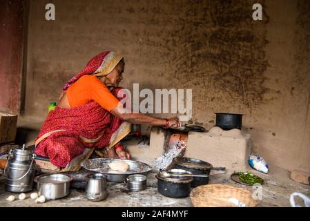 CHIKHALDARA, MAHARASHTRA - Agosto 28, 2018: Un misterioso vecchio donna fare e cucina / cottura di alimenti freschi in un villaggio rurale in una cucina vintage u Foto Stock