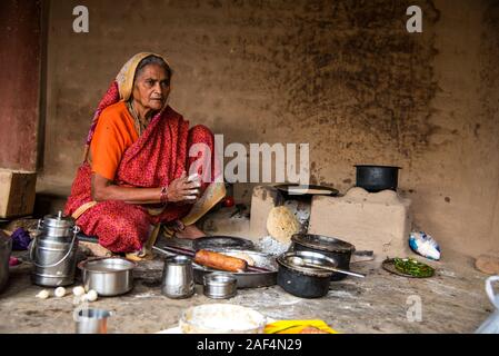 CHIKHALDARA, MAHARASHTRA - Agosto 28, 2018: Un misterioso vecchio donna fare e cucina / cottura di alimenti freschi in un villaggio rurale in una cucina vintage u Foto Stock