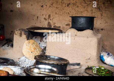 CHIKHALDARA, MAHARASHTRA - Agosto 28, 2018: Un misterioso vecchio donna fare e cucina / cottura di alimenti freschi in un villaggio rurale in una cucina vintage u Foto Stock