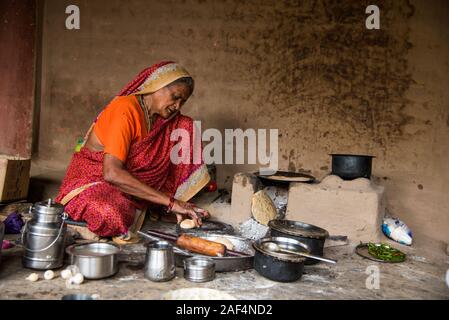 CHIKHALDARA, MAHARASHTRA - Agosto 28, 2018: Un misterioso vecchio donna fare e cucina / cottura di alimenti freschi in un villaggio rurale in una cucina vintage u Foto Stock
