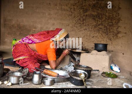 CHIKHALDARA, MAHARASHTRA - Agosto 28, 2018: Un misterioso vecchio donna fare e cucina / cottura di alimenti freschi in un villaggio rurale in una cucina vintage u Foto Stock