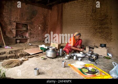 CHIKHALDARA, MAHARASHTRA - Agosto 28, 2018: Un misterioso vecchio donna fare e cucina / cottura di alimenti freschi in un villaggio rurale in una cucina vintage u Foto Stock