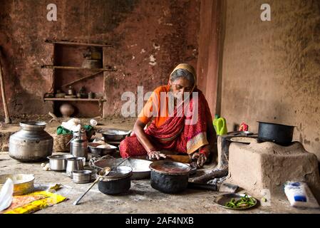 CHIKHALDARA, MAHARASHTRA - Agosto 28, 2018: Un misterioso vecchio donna fare e cucina / cottura di alimenti freschi in un villaggio rurale in una cucina vintage u Foto Stock