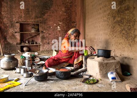 CHIKHALDARA, MAHARASHTRA - Agosto 28, 2018: Un misterioso vecchio donna fare e cucina / cottura di alimenti freschi in un villaggio rurale in una cucina vintage u Foto Stock