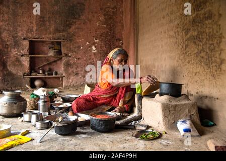 CHIKHALDARA, MAHARASHTRA - Agosto 28, 2018: Un misterioso vecchio donna fare e cucina / cottura di alimenti freschi in un villaggio rurale in una cucina vintage u Foto Stock