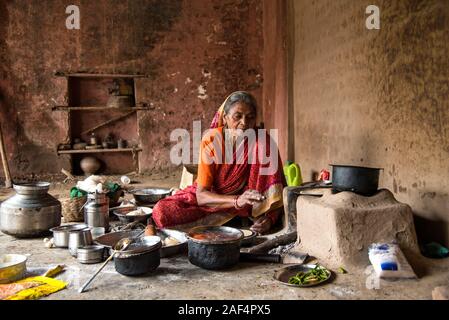 CHIKHALDARA, MAHARASHTRA - Agosto 28, 2018: Un misterioso vecchio donna fare e cucina / cottura di alimenti freschi in un villaggio rurale in una cucina vintage u Foto Stock