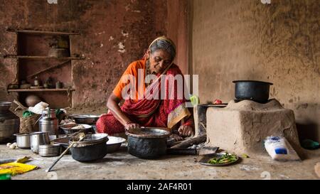CHIKHALDARA, MAHARASHTRA - Agosto 28, 2018: Un misterioso vecchio donna fare e cucina / cottura di alimenti freschi in un villaggio rurale in una cucina vintage u Foto Stock