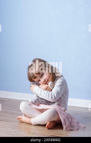 Ragazza abbracci un gatto Fluffy giocattolo seduto sul pavimento. Cancella sfondo blu e copia di spazio sulla parte superiore. Foto Stock