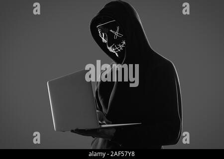 Ritratto di un anonimo uomo in una felpa con cappuccio nero e maschera al neon hacking in un computer. Studio shot. Foto Stock