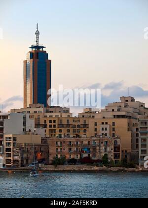Vecchio blocco di appartamenti sul lungomare di Malta offuscata da un moderno grattacielo in background Foto Stock