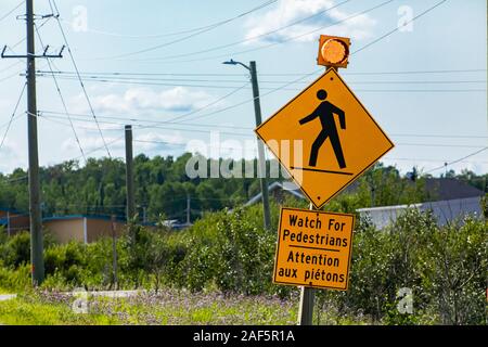 Avviso per i pedoni, avvertimento cartello stradale, guardare per i pedoni cartello bilingue francese e inglese, con luce gialla, Canadian area rurale sullo sfondo Foto Stock