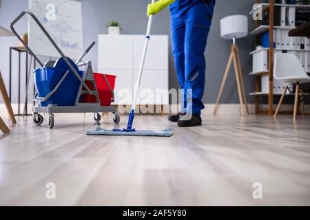 Felice Giovane la pulizia del pavimento con Mop in ufficio moderno Foto Stock