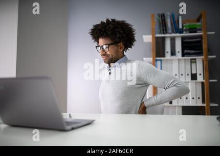 Giovane imprenditore con Backpain seduti su una sedia al lavoro Foto Stock