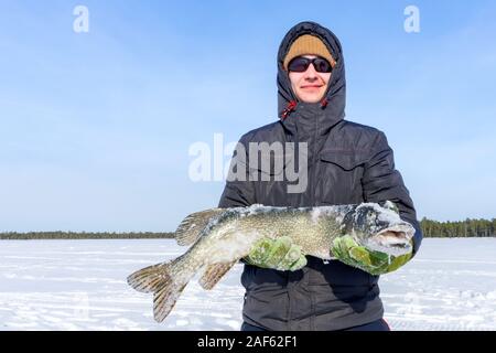 Giovane maschio millennial fisherman tenendo il grande pesce luccio del nord, e del trofeo. Pesca d'inverno. La pesca in inverno Foto Stock