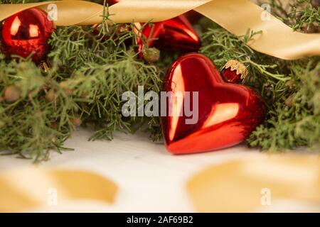 Close up di un natale baubles rosso con messa a terra con forma attorno a rami di pino, baubles rosso e oro in raso nastro su legno con sfondo bokeh effe Foto Stock