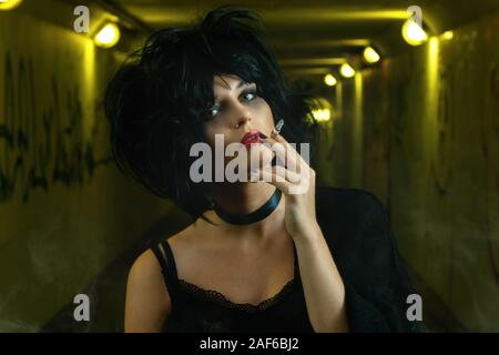 Freaky donna con i capelli neri di fumare una sigaretta nel buio metropolitana Foto Stock