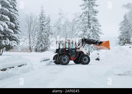 Il trattore rimozione neve invernale da strada.Grande trattore rosso con Snow Plough livellatrice cancella coperta di neve strada in montagna, lago Weissensee, Alpi, Austria Foto Stock