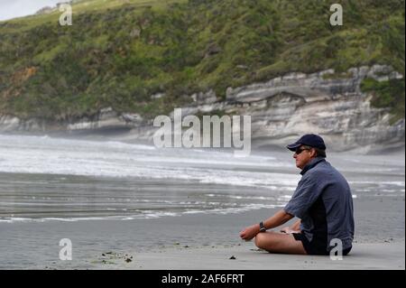 Un uomo è seduto nella posizione del loto che guarda al mare Foto Stock