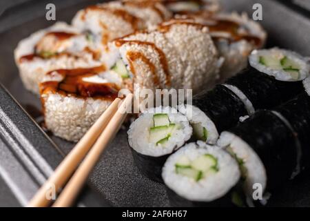 Rotoli di Sushi con crema di formaggio, nori e coperto di cetriolo con anguille, i semi di sesamo e salsa di caramello. messa a fuoco selettiva Foto Stock