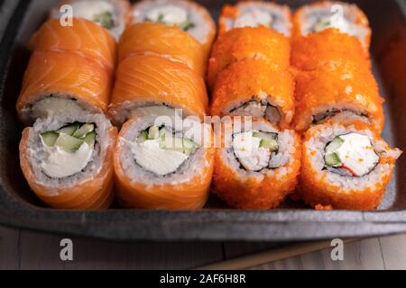 Set di sushi assortiti conservati in una scatola nera su un tavolo di legno. California e rotoli di Philadelphia Foto Stock