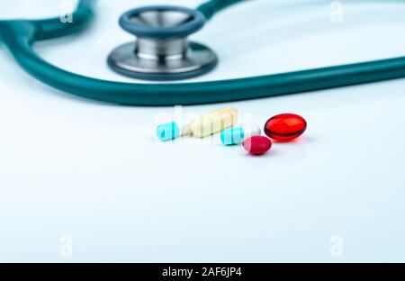 Uno stetoscopio con blu-bianco, capsule morbido rosso capsula di gel di pillole, e rosso compresse rotonde sulla tabella di medico o infermiere desk. Delle cure mediche e medicine Foto Stock