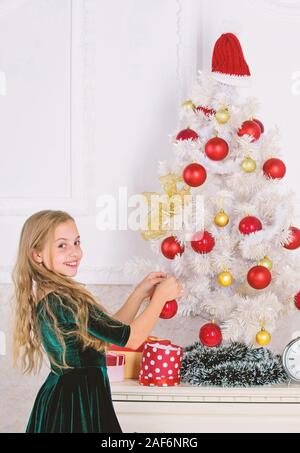 Bambino mettere ornamento di Natale a sfera artificiale su albero bianco. Top Natale che decora le idee per la stanza dei ragazzi. I bambini possono illuminare albero di natale creando i propri ornamenti. Ragazza festeggiano il Natale. Foto Stock