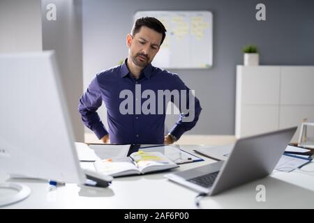 Imprenditore avente dolore alla schiena mentre è seduto alla scrivania in ufficio Foto Stock