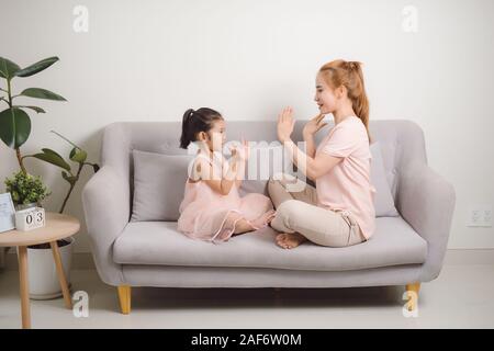 Felice giovane donna giocando battimani gioco con bambino femmina mentre è seduto in soggiorno Foto Stock