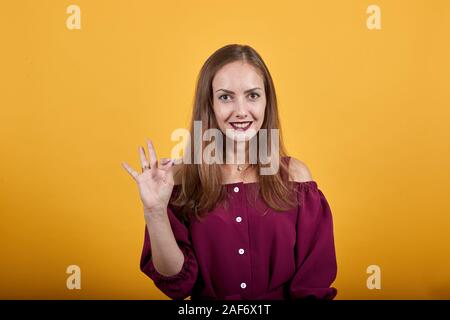 Donna in Borgogna bluse su sfondo arancione mostra segno OK con sorriso Foto Stock