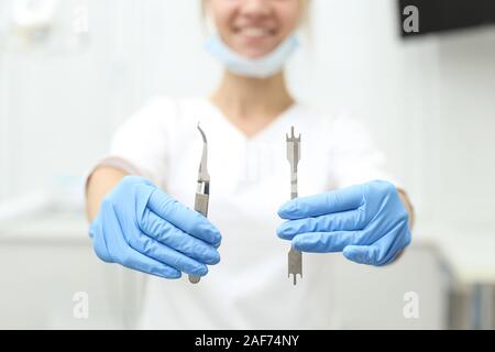 Attraente dentista femmina detiene strumenti nelle sue mani e nel suo sorriso affascinante a. Messa a fuoco selettiva. Foto Stock