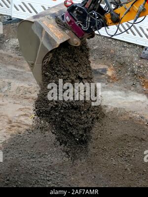 Una cucchiaia escavatore scarica un carico di sporcizia su una strada sito in costruzione Foto Stock