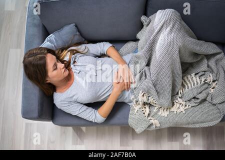 Angolo di Alta Vista della giovane donna che soffre di Stomachache sul divano di casa Foto Stock