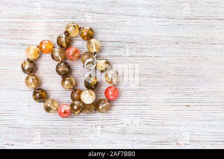 Vista dall'alto di aggrovigliarsi sfaccettato collana di agata grigia su tavola di legno con copyspace Foto Stock