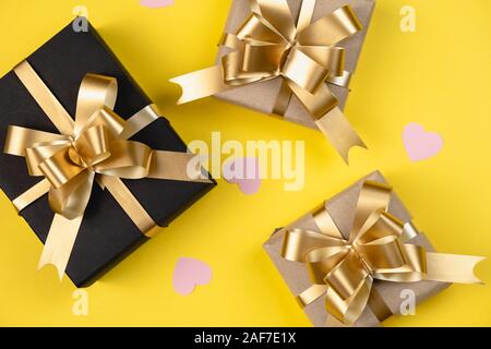 Sfondo di vacanza. Vari fatti a mano scatole regalo decorata con cuore rosa coriandoli su sfondo giallo. Stile minimal e il giorno di San Valentino del concetto. Fla Foto Stock