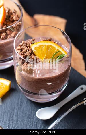 Cibo sano concetto Chia cioccolato budino arancione con cereali e semi di zucca topping nei bicchieri Foto Stock