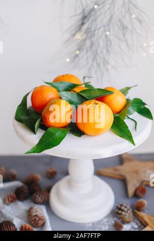 Tangerini arancione su sfondo grigio nel nuovo anno con decor di marrone pigne e foglie verdi. Deliziosi dolci clementine. Decorazione di natale con Foto Stock