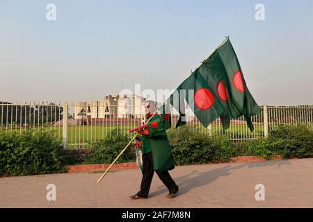 Dacca in Bangladesh - Dicembre 08, 2019: un venditore ambulante bengalese vende bandiere nazionali di fronte al parlamento nazionale edificio a Dhaka in Bangl Foto Stock