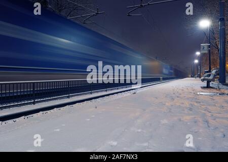 Passing freight train in blurred motion at train station on a winter night. Transportation and logistic service concepts Foto Stock