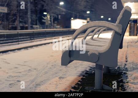 Vacante in panchina coperta di neve in corrispondenza di un vuoto che la stazione ferroviaria di notte. Attesa, di solitudine e di concetti di trasporto Foto Stock