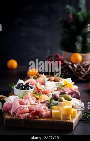 Antipasto piatto con prosciutto cotto, prosciutto, salame, formaggio, cracker e olive su uno sfondo di legno. Tavola del Natale. Foto Stock