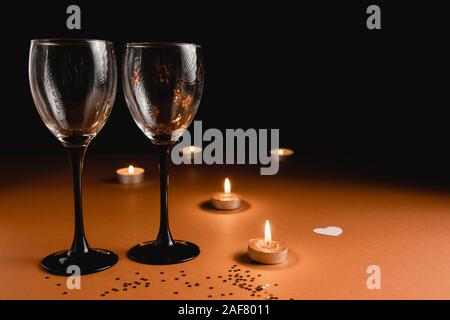 Sfondo di vacanza. Il tintinnio di due bicchieri di vino, candela, coriandoli su Orange e sfondo nero. Stile minimal e il giorno di San Valentino del concetto. Piatto, laici co Foto Stock