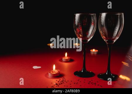 Sfondo di vacanza. Il tintinnio di due bicchieri di vino, candela, coriandoli sul rosso e sfondo nero. Stile minimal e il giorno di San Valentino del concetto. Laici piana, copia Foto Stock