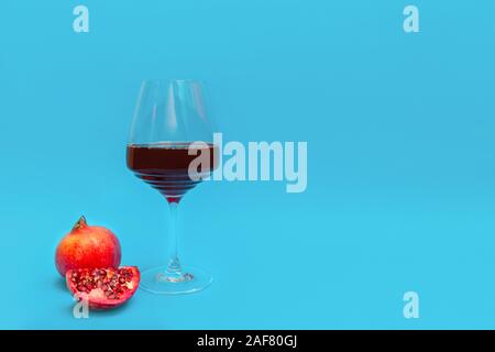 Melograno rosso vino in un bicchiere di vino con un fresco e melograno e una fetta su sfondo blu. Immagine con spazio di copia Foto Stock