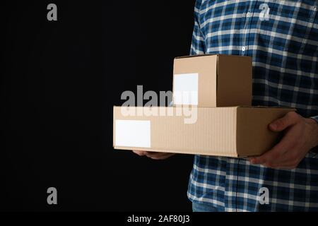 Uomo in camicia tenere caselle bianche su sfondo nero, spazio per il testo Foto Stock