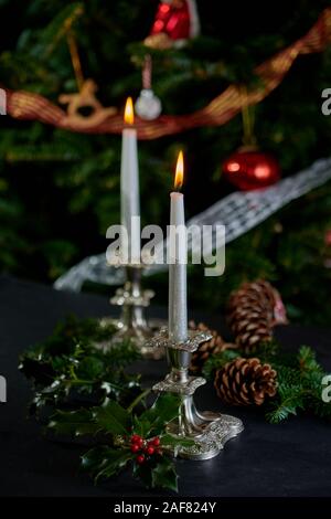 Flaming candele in argento antico portacandele con albero di Natale decorato a sfondo. Foto Stock