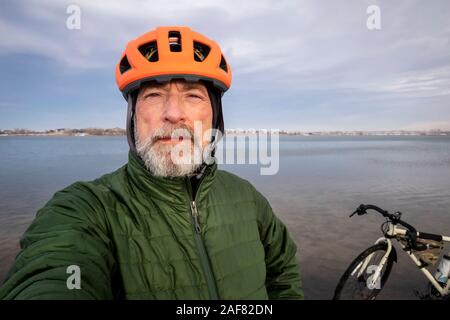 Ritratto ambientale del maschio senior indossando il casco, passamontagna e down jacket per il ciclismo invernale, Boyd il lago del Parco statale nel nord del Colorado Foto Stock