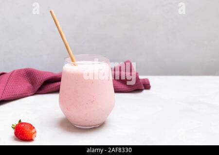 Tradizionale Indiano di yogurt drink Strawberry Lassi in un bicchiere di vetro sul cemento sfondo neutro, spazio di copia Foto Stock